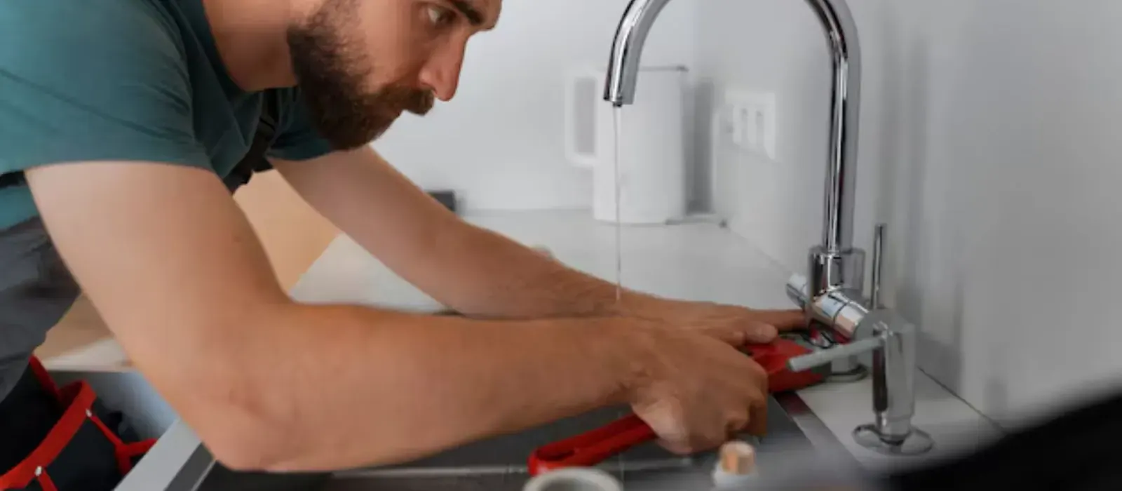 Plumber tightening a kitchen faucet with a pipe wrench, faucet repair in Clearfield, UT